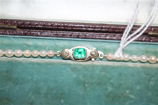 A single strand graduated cultured pearl necklace with an emerald and diamond set white metal clasp, approx. 35cm.